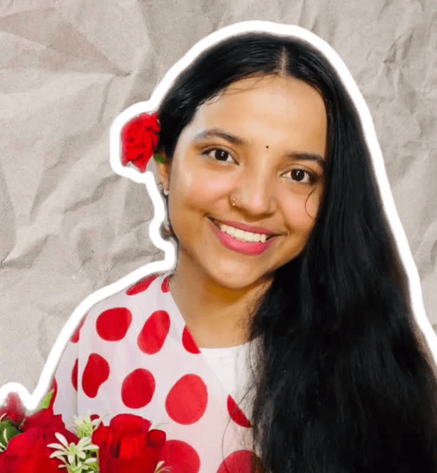 Shivangi smiling in a red polka-dot top with roses tucked behind her ear and in her hands